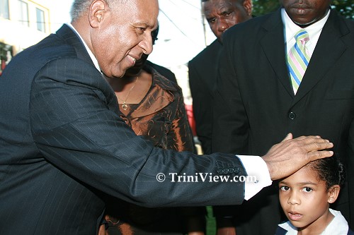 Prime Minister Patrick Manning lays hand on child
